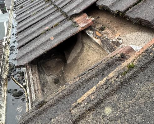 Roof inspection revealing hidden eaves line defects Lifted roof tiles showing hidden eaves line defects near a gutter