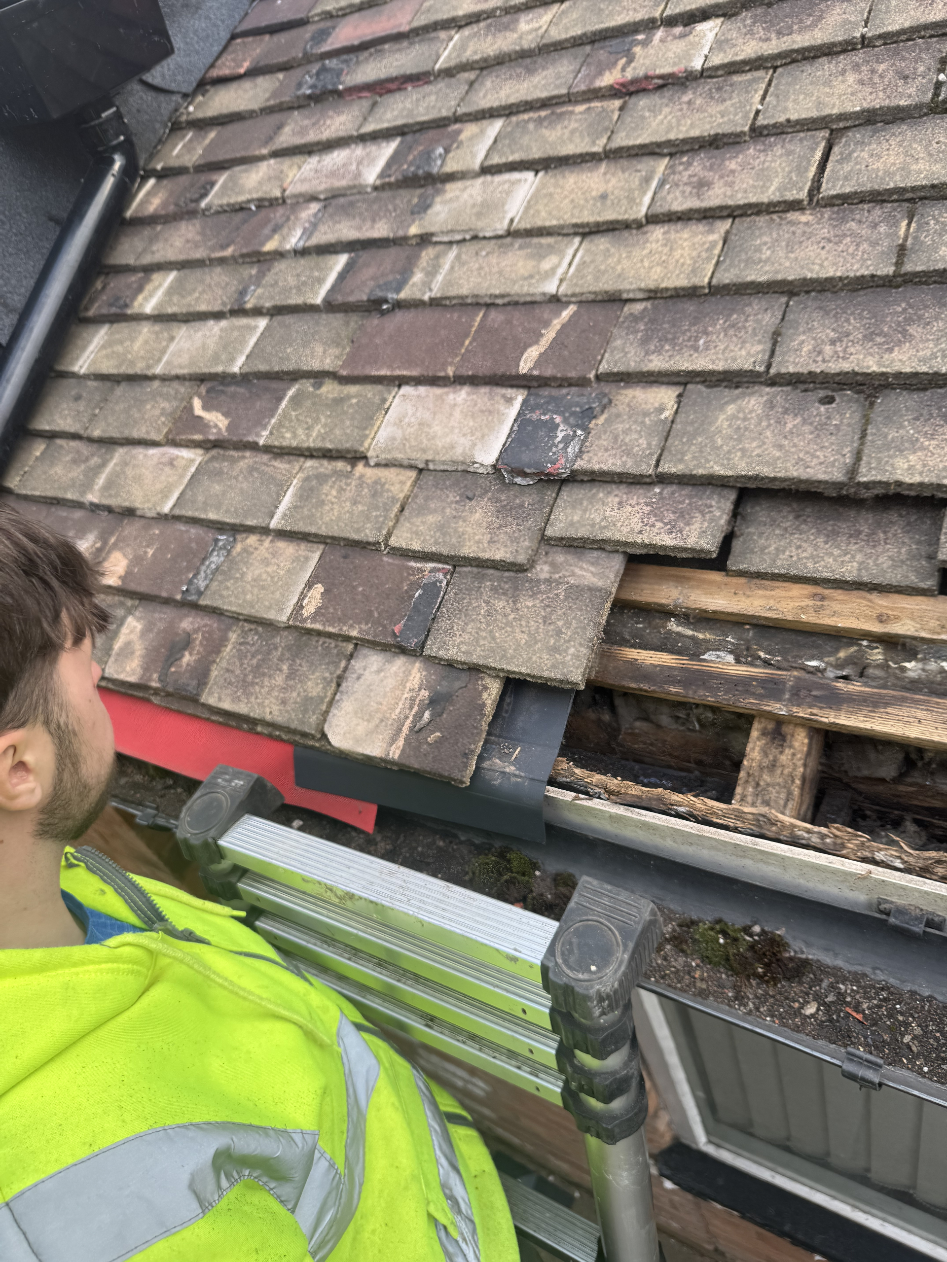 Roofing contractor inspecting hidden timber damage beneath lifted roof tiles at the eaves