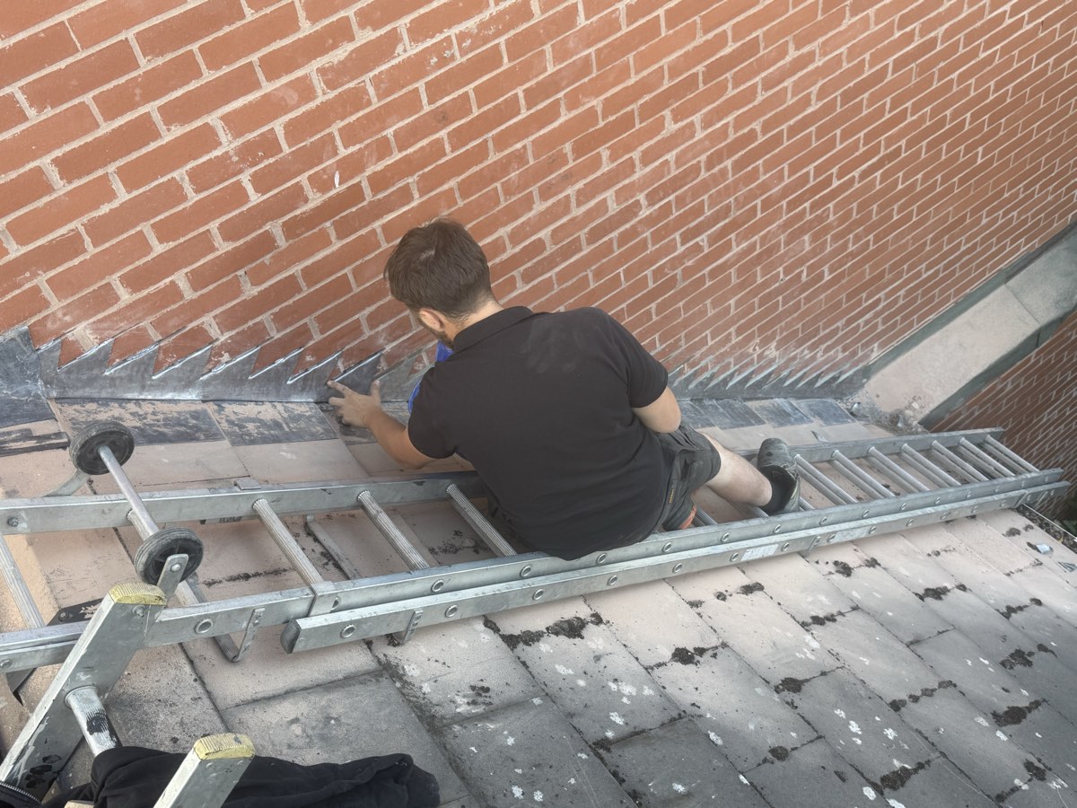 Roofer installing stepped lead flashing where a tiled roof meets a brick wall in Birmingham